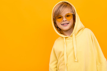 Handsome boy in yellow hoodie smiles and gesticulates isolated on orange background