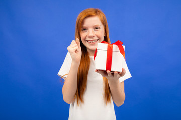 happy joyful teenage girl with red hair received a birthday present on a blue studio background