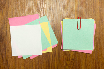 Blank colorful note paper with red paper clip on wooden desk.