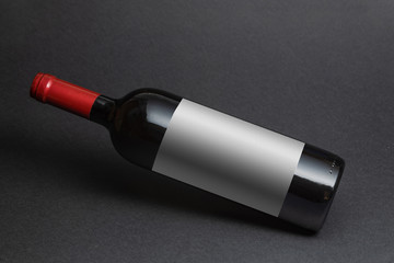 Red wine bottle mockup with white label on black background.