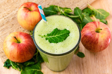 Green smoothie drink surrounded by apples & kale on wooden table