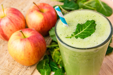 Green smoothie drink surrounded by apples & kale on wooden table