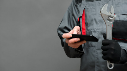 A worker with a mobile phone and wrench in the hands close up.