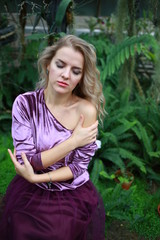  beautiful girl with long white hair in violet velvet top and lilac light fanin skirt enjoys nature in the garden