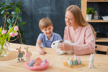 Fototapeta premium Smiling mother stroking fluffy rabbit together with excited son while celebrating Easter