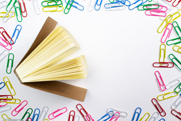 Colorful paper clips around and diary with cardboard cover in the centre of composition with free space isolated on white.