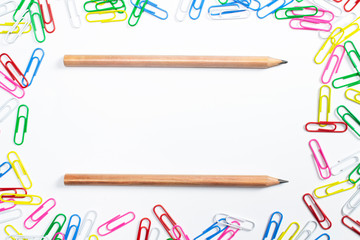Colorful paper clips around and wooden pencils in the centre of composition with free space isolated on white.