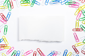 Colorful paper clips and torned paper frame in the centre of composition isolated on white.