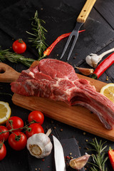 Raw beef antricot on a wooden board. Composition with rosemary, hot pepper and other spices for cooking meat. A look from above.