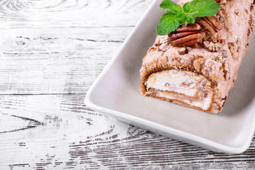 Meringue roulade with pecan nuts and cream cheese filling on the ceramic platter on the white wooden table