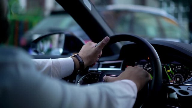 Close up view from back seat businessman in white shirt holding hands on steering wheel while driving vehicle automobile waiting for green light. Blurred city view behind windshield while car moving 