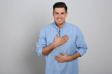 Handsome grateful man with hands on chest against light grey background