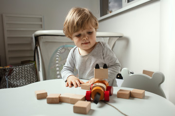 Beautiful toddler play with a wodden toys at home. Child play at the table in the baby room.  Funny baby. Lifestyle.