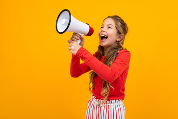 European teenager girl shouting news in a megaphone and stands sideways on a yellow studio background