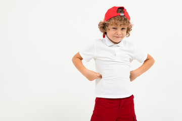 Caucasian boy in white t-shirt, red cap, red shorts is unhappy isolated on white background