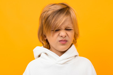 Handsome boy in white hoodie smiles and gesticulates isolated on orange background