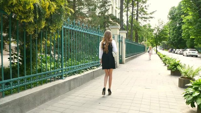 Slow motion video.Back view business woman walking on the street in modern urban city. Female with blond hair walks in the morning.