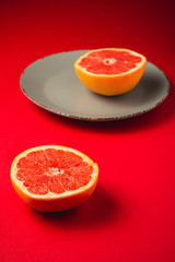 Fototapeta na wymiar Grapefruit near to grey plate with fruit half of fruit, tropical creative minimal food concept, on vibrant red background, lush lava, angle view selective focus
