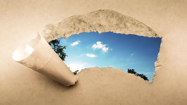 Creative 4k time laps video of fast moving clouds in the blue sky at sunset witn sunflare that are visible through a hole with torn edges in old retro grunge vintage paper.