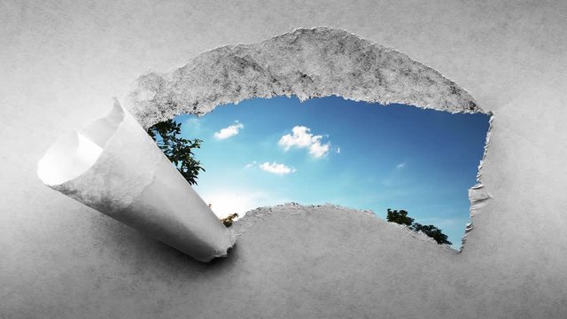 Creative 4k time laps video of fast moving clouds in the blue sky at sunset witn sunflare that are visible through a hole with torn edges in old retro grunge vintage paper.