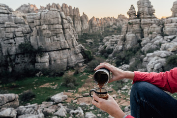 Young woman explorer making coffee in a cup on the mountain. Concept of adventure, excursion and trips.