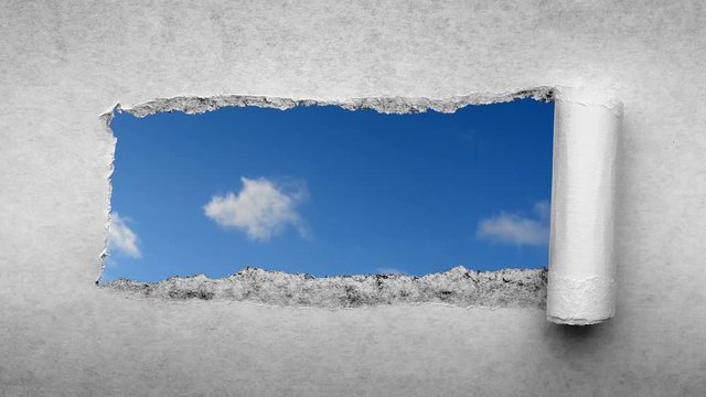 Creative 4k time laps video of fast moving clouds in the blue sky that are visible through a hole with torn edges in old retro grunge vintage paper.