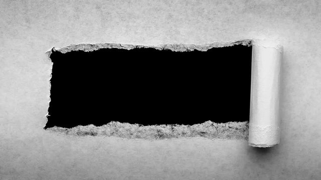 Creative 4k time laps video of a glowing full moon in the night sky with floating clouds, which is visible through a hole with torn edges in old retro grunge vintage paper.