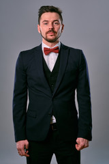 Young business man in classic black suit, white shirt and red bow-tie. Posing against a gray studio background. Mock up, copy space. Close-up.