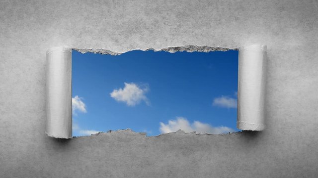 Creative 4k time laps video of fast moving clouds in the blue sky that are visible through a hole with torn edges in old retro grunge vintage paper.