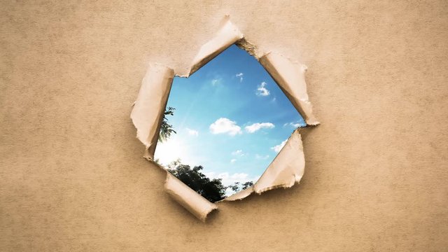 Creative 4k time laps video of fast moving clouds in the blue sky that are visible through a hole with torn edges in old retro grunge vintage paper.