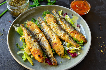 Grilled fish in a gray plate. Small fried fish and salad dressing. Close-up.