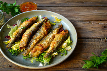 Grilled fish in a gray plate. Small fried fish and salad dressing. Close-up.