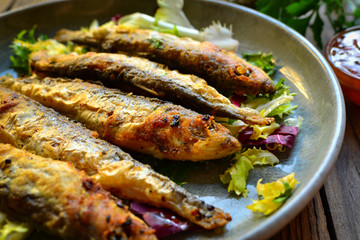 Grilled fish in a gray plate. Small fried fish and salad dressing. Close-up.