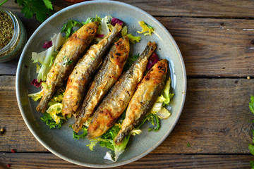 Grilled fish in a gray plate. Small fried fish and salad dressing. Top view. Wood background
