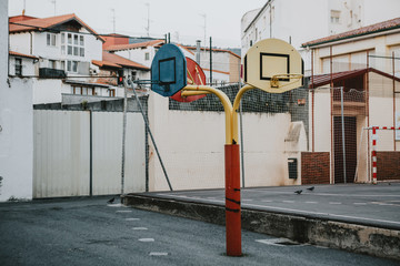 Empty school asphalt playground in the backyard with three color baskets for basketball and part for handball in background in the center of spain town Castro Urdiales during the summer morning.