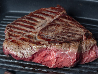 A large piece of juicy fresh beef fried on one side in a pan-grill. Stripes-rare, the juice from the meat. Close up, front view