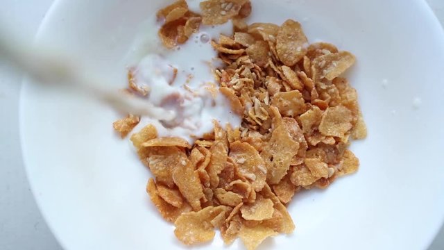  Milk pouring into bowl of cornflakes, slow motion. Healthy breakfast of cereal with milk, close up. 