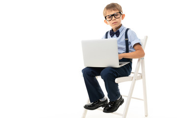 Clever young caucasian teenager sits on a chair and do homework with his laptop on white background