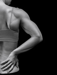 Bodybuilder woman suffers from pain in her back after workout, black background