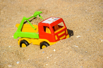 Children's toy car, colorful plastic lorry on beach sand.