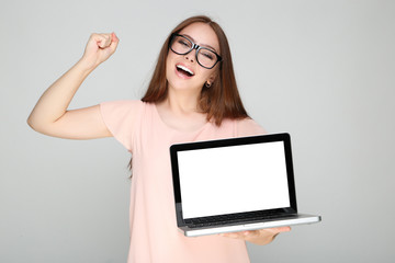 Young woman showing blank laptop screen on grey background
