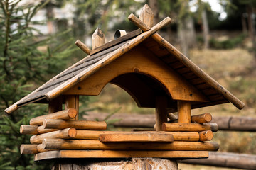 Birdhouse on a tree hanging from a branch. Wooden birdhouse made of small logs. Birdhouse on blurred city background. Handcrafted log cabin birdhouse. Save animals