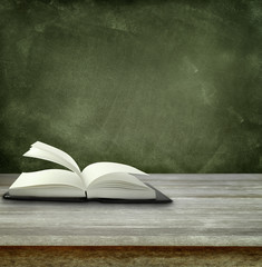 Open book on table and chalkboard in classroom