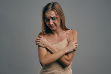 Fototapeta premium Blonde girl with bruises on her face, pressed her hands to chest, posing on gray studio background. Domestic violence, abuse. Close-up, copy space.