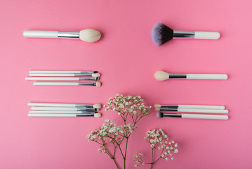 white makeup brushes and white small flowers on a pink background