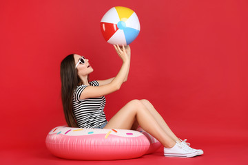 Young girl with colorful ball and inflatable donut on red background