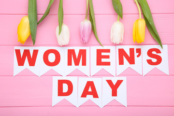 Text Womens Day with tulip flowers on pink wooden table