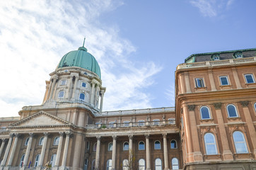 Buda Castle in Budapest, Hungary with light blue sky and clouds above. Historical castle and palace complex of the Hungarian kings. Facade with pillars, balconies and cupola. Tourist attraction