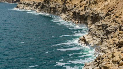 Obraz premium Beautiful cliffs cascade down into emerald water of Dead Sea. Salt crystals show in strips level of leaving water 2011 year. Dead Sea coastline in Jordan. Ecology theme. There is place for your text
