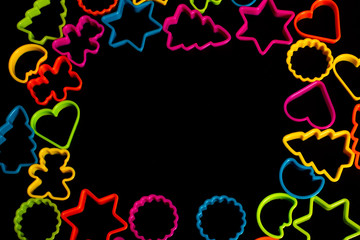 Multi-colored plastic molds of various shapes for the manufacture of cookies on a black background. Culinary concept. Flat lay with copyspace.